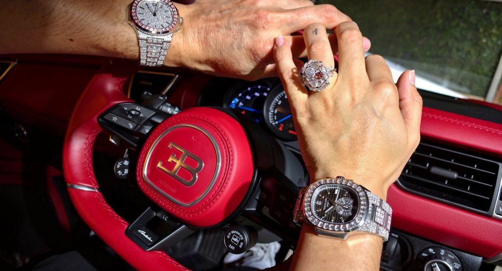 La vidéo montre les mains de Georgina Rodriguez et Cristiano Ronaldo se tenant sur le volant d'une Bugatti rouge. Les deux portent des montres de luxe incrustées de diamants, et Georgina arbore également une très grande bague en diamant. Le tableau de bord et le logo Bugatti sur le volant sont clairement visibles. Aucun visage n'est visible dans cette scène.