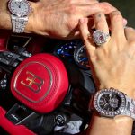 La vidéo montre les mains de Georgina Rodriguez et Cristiano Ronaldo se tenant sur le volant d'une Bugatti rouge. Les deux portent des montres de luxe incrustées de diamants, et Georgina arbore également une très grande bague en diamant. Le tableau de bord et le logo Bugatti sur le volant sont clairement visibles. Aucun visage n'est visible dans cette scène.